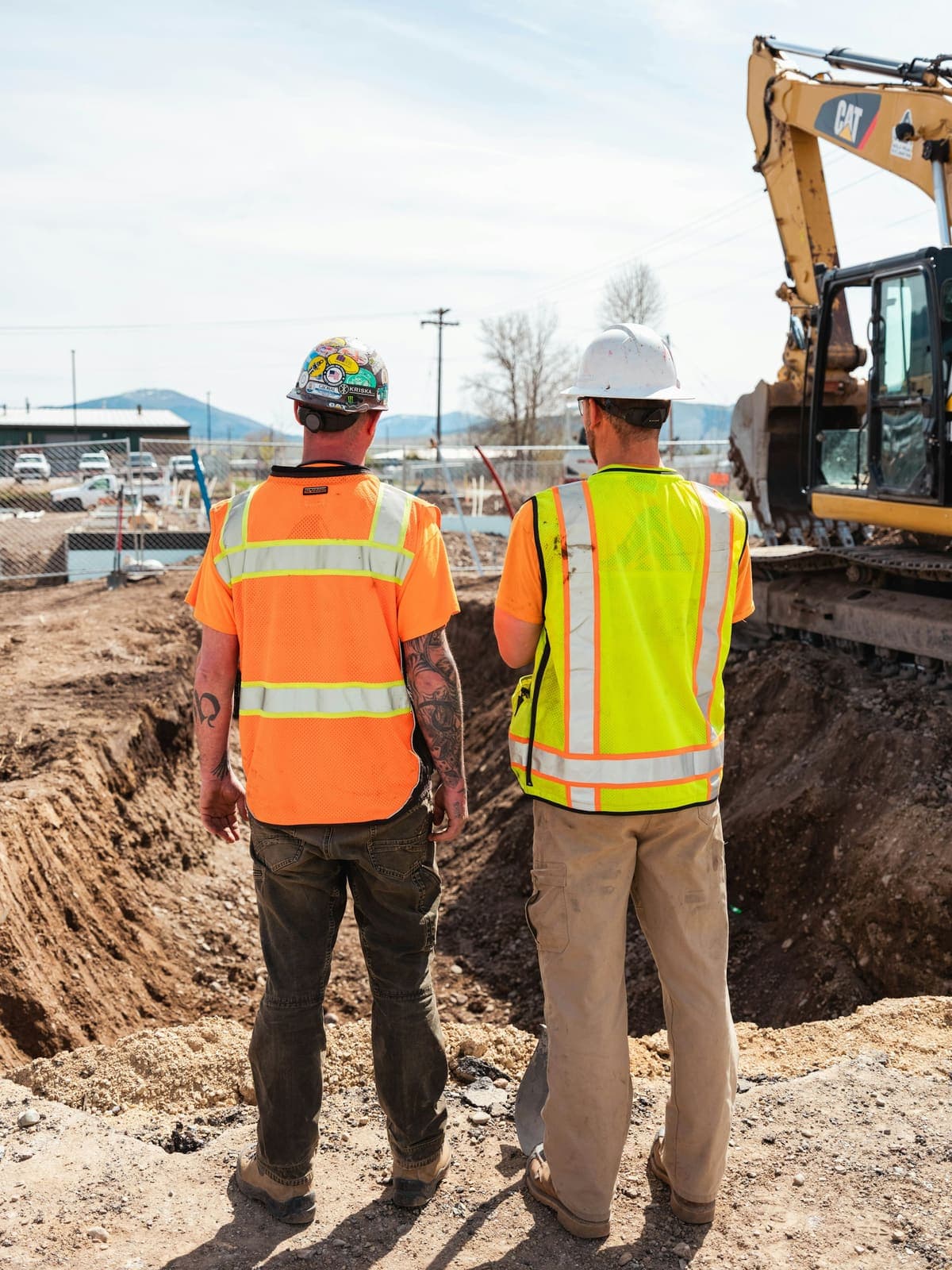 Two construction workers in high-visibility jackets at an excavation site